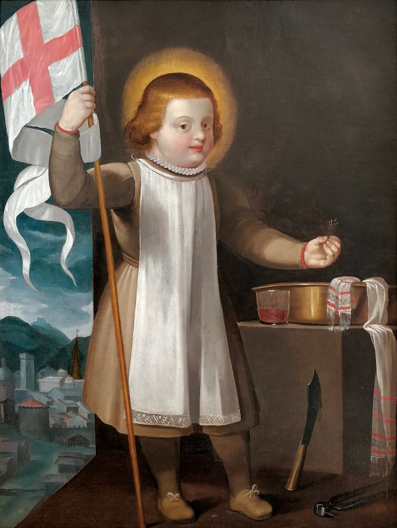 A painting of a child saint with a golden halo, wearing a brown tunic and a white apron-like garment. The child holds a white flag with a red cross in the left hand and small crosses or flowers in the right hand. To the right, a table holds a brass basin with a glass of red liquid and a white cloth with red stripes draped over the edge. A curved knife and tongs rest on the floor nearby. In the background, a mountainous landscape with a small town is visible.